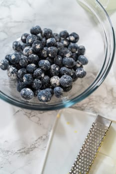 Integrating ingredients in a glass bowl, adeptly stirring with a whisk to craft a tantalizing lemon-blueberry bundt cake.