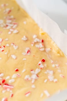 Removing candy cane fudge from a square cheesecake pan lined with parchment.