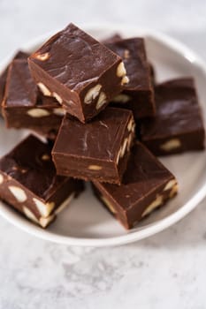 Homemade chocolate macadamia fudge square pieces on a white plate.