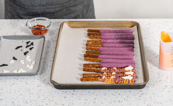 Dipping pretzel rods into melted chocolate to make Halloween chocolate-covered pretzel rods.