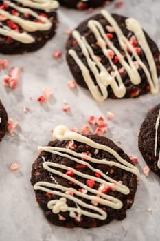 Freshly baked chocolate cookies with peppermint chips with a white chocolate drizzle on top.