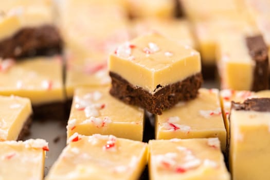 Cutting candy cane fudge with a large kitchen knife into square pieces on a white cutting board.