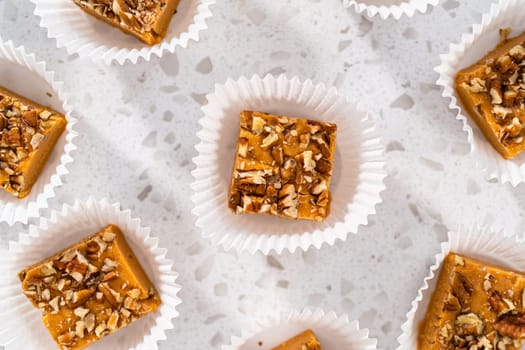 Homemade pumpkin spice fudge square pieces in white paper cupcake liners on a kitchen counter.