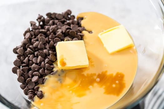 Melting chocolate chips and other ingredients in a glass mixing bowl over boiling water to prepare chocolate hazelnut fudge.