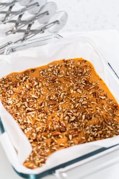 Freshly made homemade pumpkin spice fudge in a square glass baking pan lined with parchment paper.