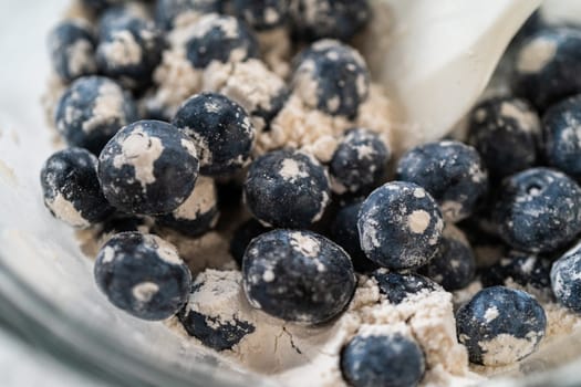 Integrating ingredients in a glass bowl, adeptly stirring with a whisk to craft a tantalizing lemon-blueberry bundt cake.