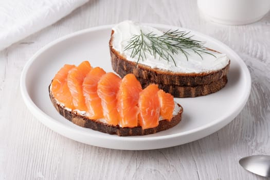 Rye sandwich with salmon and cream cheese on white wooden table.