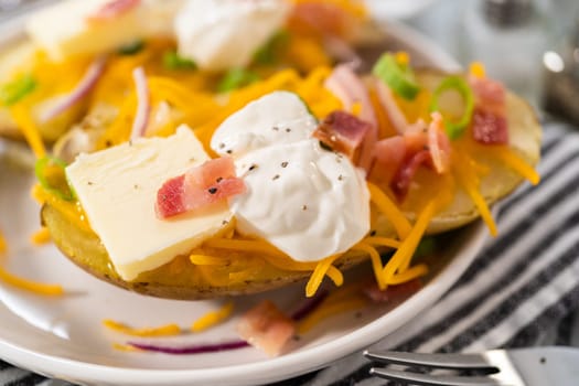 Pressure Cooker Baked Potatoes. Garnished large baked potatoes with butter, sour cream, cheese, and bacon bits on a white plate.