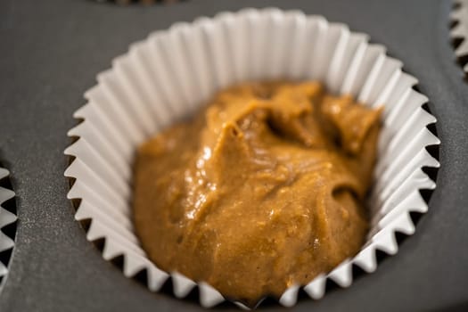 Scooping cupcake batter with a dough scoop into cupcake foil liners to bake gingerbread cupcakes.