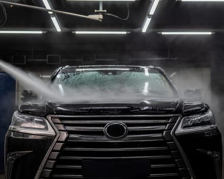 A man washes foam off a black car with water at a car wash