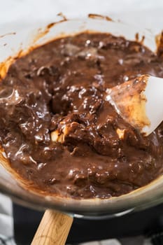 Melting white chocolate chips and other ingredients in a glass mixing bowl over boiling water to prepare chocolate macadamia fudge.