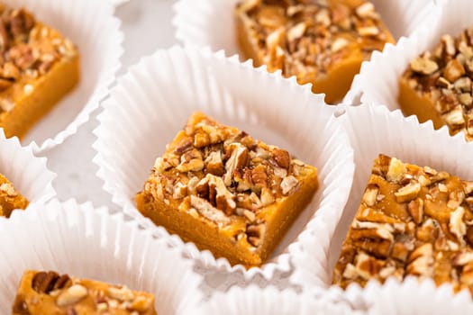 Homemade pumpkin spice fudge square pieces in white paper cupcake liners on a kitchen counter.