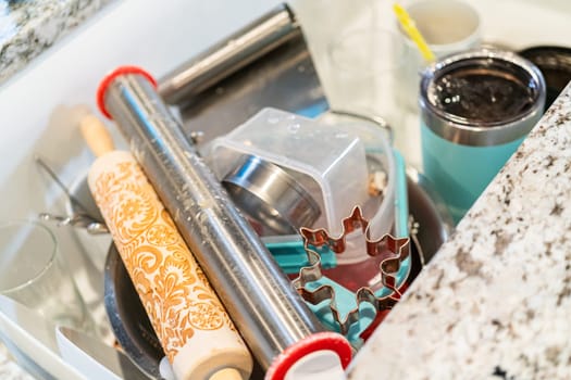 After a fun day of baking snowflake sugar cookies, the kitchen sink is filled with a pile of dirty dishes waiting to be cleaned.