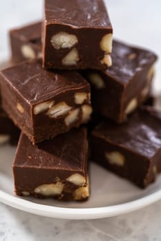 Homemade chocolate macadamia fudge square pieces on a white plate.