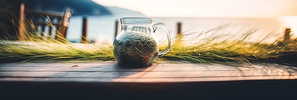 A glass pitcher with a green plant inside is sitting on a wooden table by the ocean. The scene is serene and peaceful, with the ocean in the background and the pitcher as the focal point