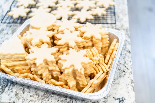 Carefully stacking the beautifully crafted snowflake-shaped sugar cookies into a foil pan, ready for freezing as delightful Christmas treats.