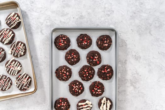 Flat lay. Drizzling melted white chocolate over freshly baked chocolate cookies with peppermint chips.