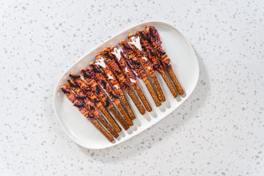 Flat lay. Halloween chocolate-covered pretzel rods with sprinkles on a white serving plate.