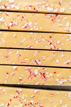 Cutting candy cane fudge with a large kitchen knife into square pieces on a white cutting board.