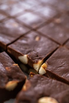 Cutting chocolate macadamia fudge with a large kitchen knife into square pieces on a white cutting board.