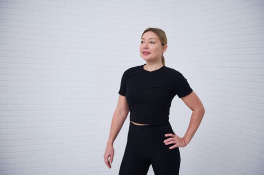 Beautiful Caucasian athletic woman 30s in black sportswear, confidently looking way, isolated over white wall background with copy advertising space