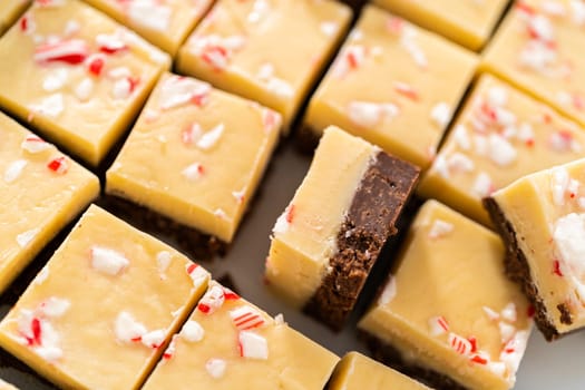 Cutting candy cane fudge with a large kitchen knife into square pieces on a white cutting board.