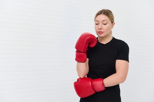 Caucasian young blonde woman 30s, wearing red boxing gloves, isolated over white wall background for copy advertising space. athletic woman ready for boxing training. Sport, discipline, endurance.