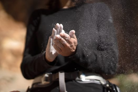 The girl is engaged in rock climbing, uses white powder of magnesia, claps her hands close-up, the woman leads an active lifestyle, climbs the mountains outdoor.