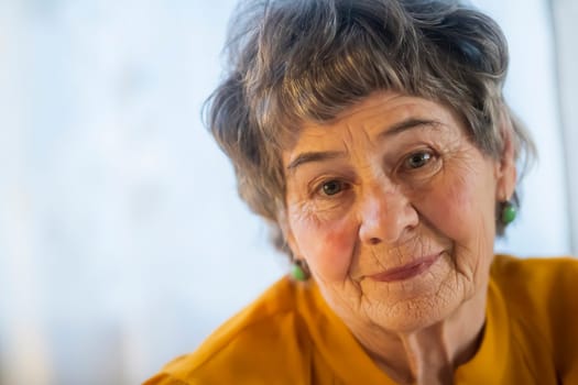 A portrait of a laughing, smiling elderly woman with gray hair and wrinkles on her face, but young at heart and leading an active lifestyle. Happy pensioner is pretty posing in her cozy home.