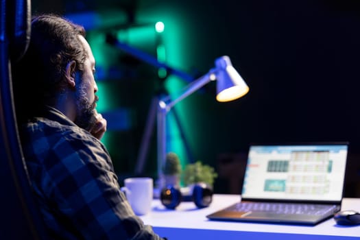 A bearded man checks economic and financial information on his portable computer. Male with hand on chin, looking at a laptop screen that displays the stock market.