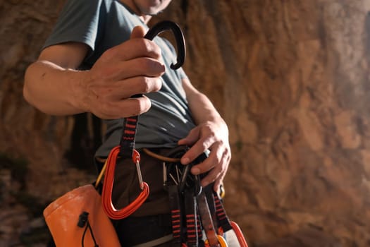 A young strong sporty man is engaged in rock climbing and mountaineering, a man's hand holds a climbing gear, a quickdraw close-up against a background of red rocks on a sunny day.