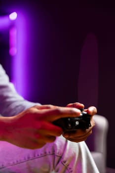 Gamer in neon lit apartment using controller to play videogame at home, close up. Man in RGB illuminated home using high tech gaming console gamepad to defeat opponents in game