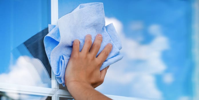 A woman's hand holds a cloth to wipe surfaces and washes the windows of her house to perfect cleanliness and freshness, a creative concept with a close-up of a reflecting sky.