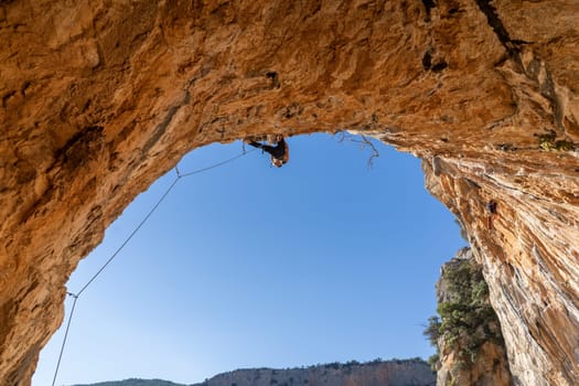 A man is professionally engaged in extreme sports, mountaineering and rock climbing, climbs the ceiling, the top of the cave against the blue sky on a sunny day in Twin Caves, Arcadia, Greece.