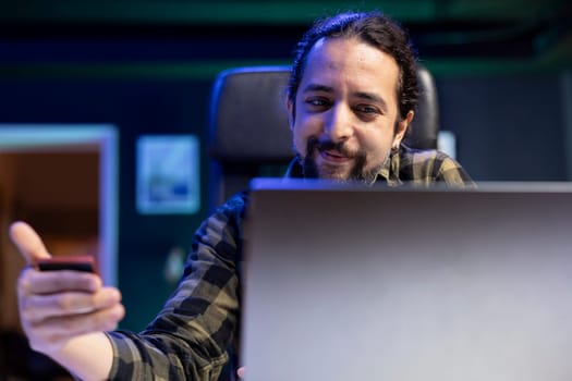 Smiling male freelancer doing internet banking on his laptop, showcasing modern trend of remote work and financial management. Positive guy grasps debit card for online purchases.