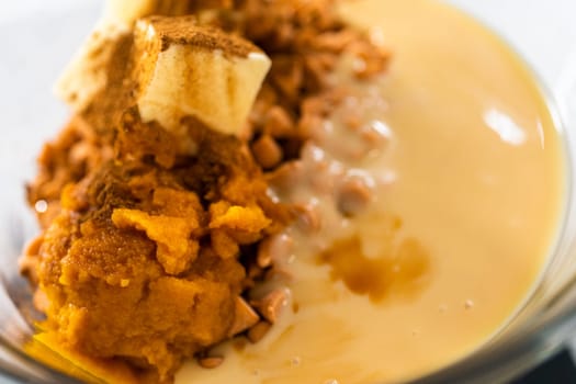 Melting chocolate chips and other ingredients in a glass mixing bowl over boiling water to prepare pumpkin spice fudge.