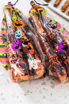 Packaging Halloween chocolate-covered pretzel rods with sprinkles into gift bags.