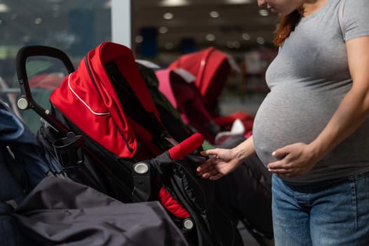 Faceless pregnant woman chooses a stroller in a children's store. Close-up of the abdomen