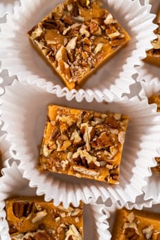 Homemade pumpkin spice fudge square pieces in white paper cupcake liners on a kitchen counter.