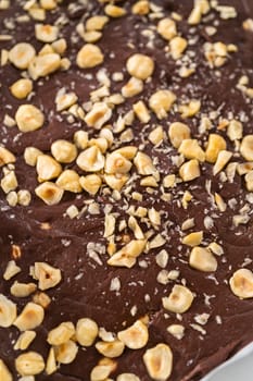 Removing chocolate hazelnut fudge from a square cheesecake pan lined with parchment.