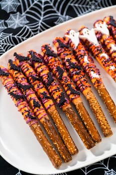 Halloween chocolate-covered pretzel rods with sprinkles on a white serving plate.