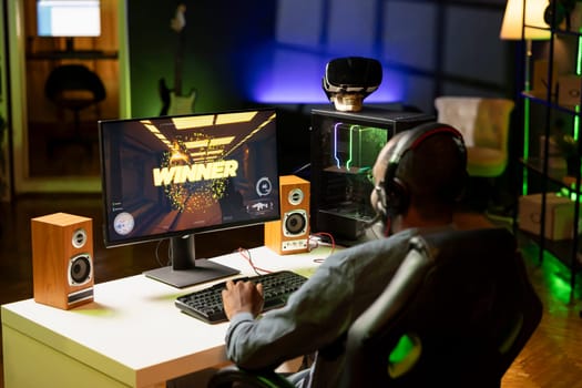 African american man feeling happy while playing videogames on computer desktop, celebrating victory. Cheerful gamer smiling after winning game on gaming PC while at home