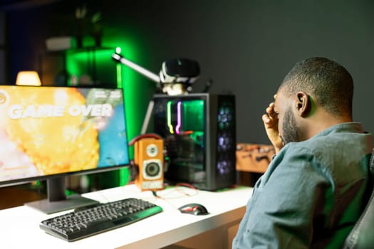 Gamer losing intense singleplayer spaceship arcade racing videogame, seeing game over screen on gaming computer monitor. Man being upset after being destroyed on difficult SF game level