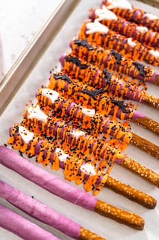 Dipping pretzel rods into melted chocolate to make Halloween chocolate-covered pretzel rods.