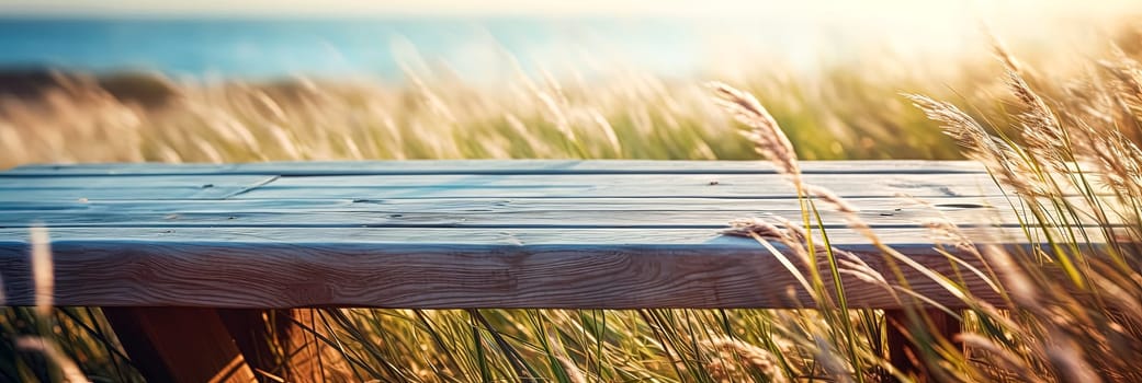 A wooden bench is sitting in a field of tall grass. The grass is blowing in the wind, creating a sense of movement and energy. The bench is empty, but it seems inviting and peaceful