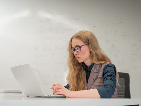 Caucasian woman scientist typing on laptop. White board with formulas