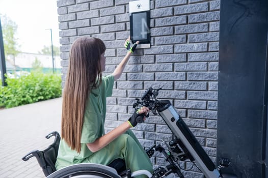 A woman in a wheelchair with an assistive device for manual control enters the entrance. Electric hand bike