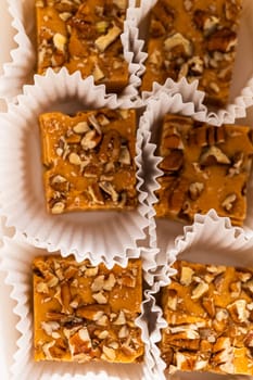 Packaging homemade pumpkin spice fudge with pecans into a white paper gift box.