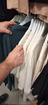 A person standing in front of a rack of shirts, holding one up for inspection.