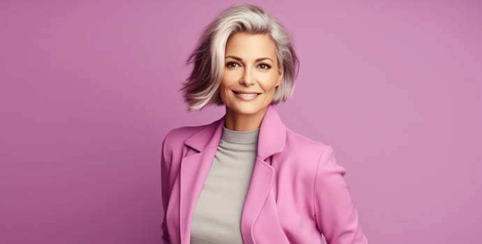 Fashion portrait of stylish happy smiling mature woman with gray hair in bright colorful clothes posing on pink studio background